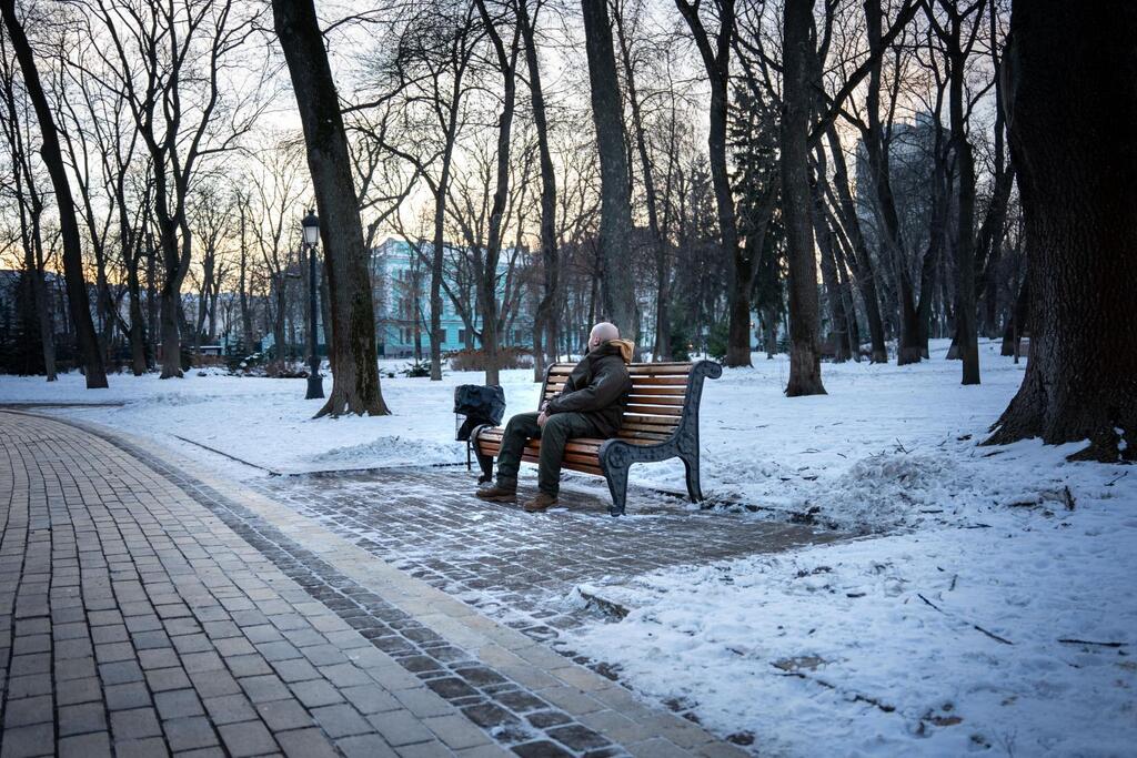 Una persona descansa en un banco de un parque ucraniano nevado durante el crepúsculo.